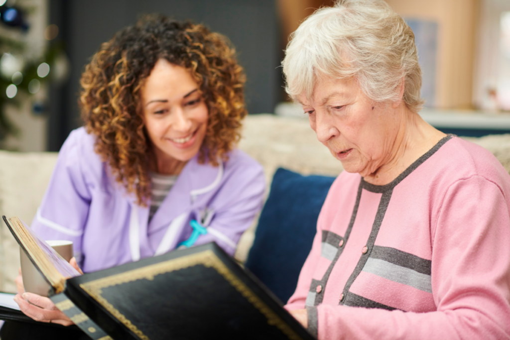 Image of a patient with dementia being shown a photo album by a carer | companion care services in kent | dementia care in kent ! care support in hythe | carer being attentive