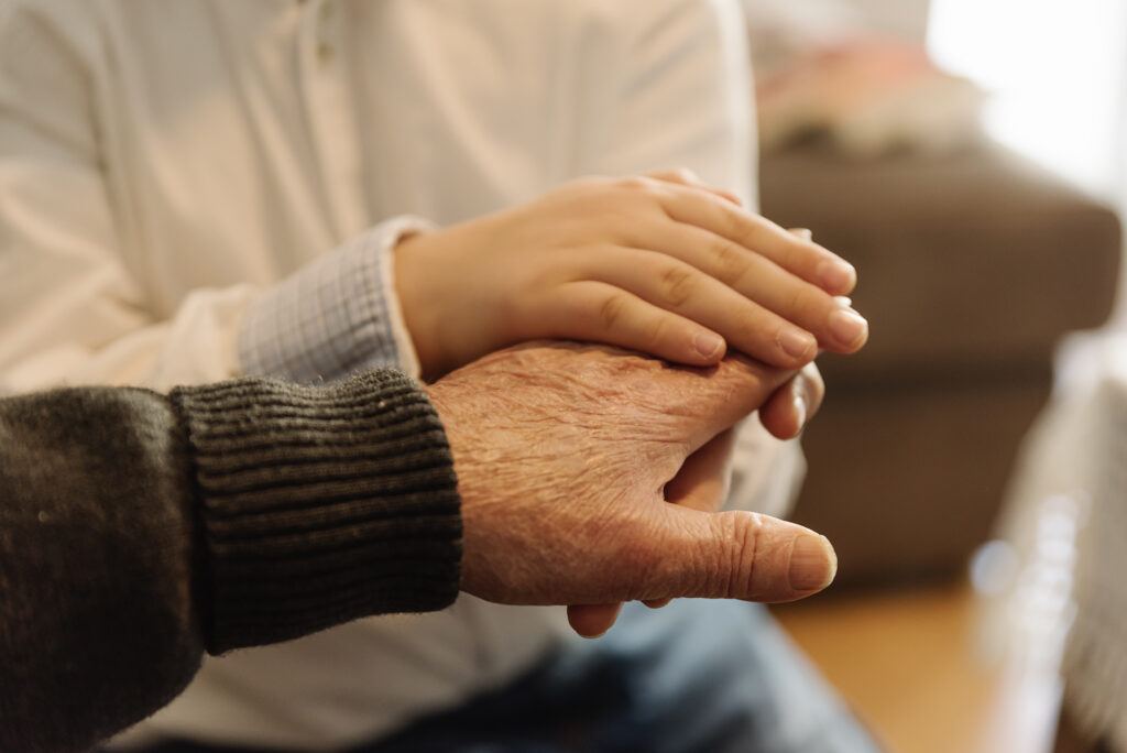 A gentle hand holding onto the hand of an elderly person, symbolizing support and care. Alt text: "Supporting the mobility of elderly loved ones with care and compassion."