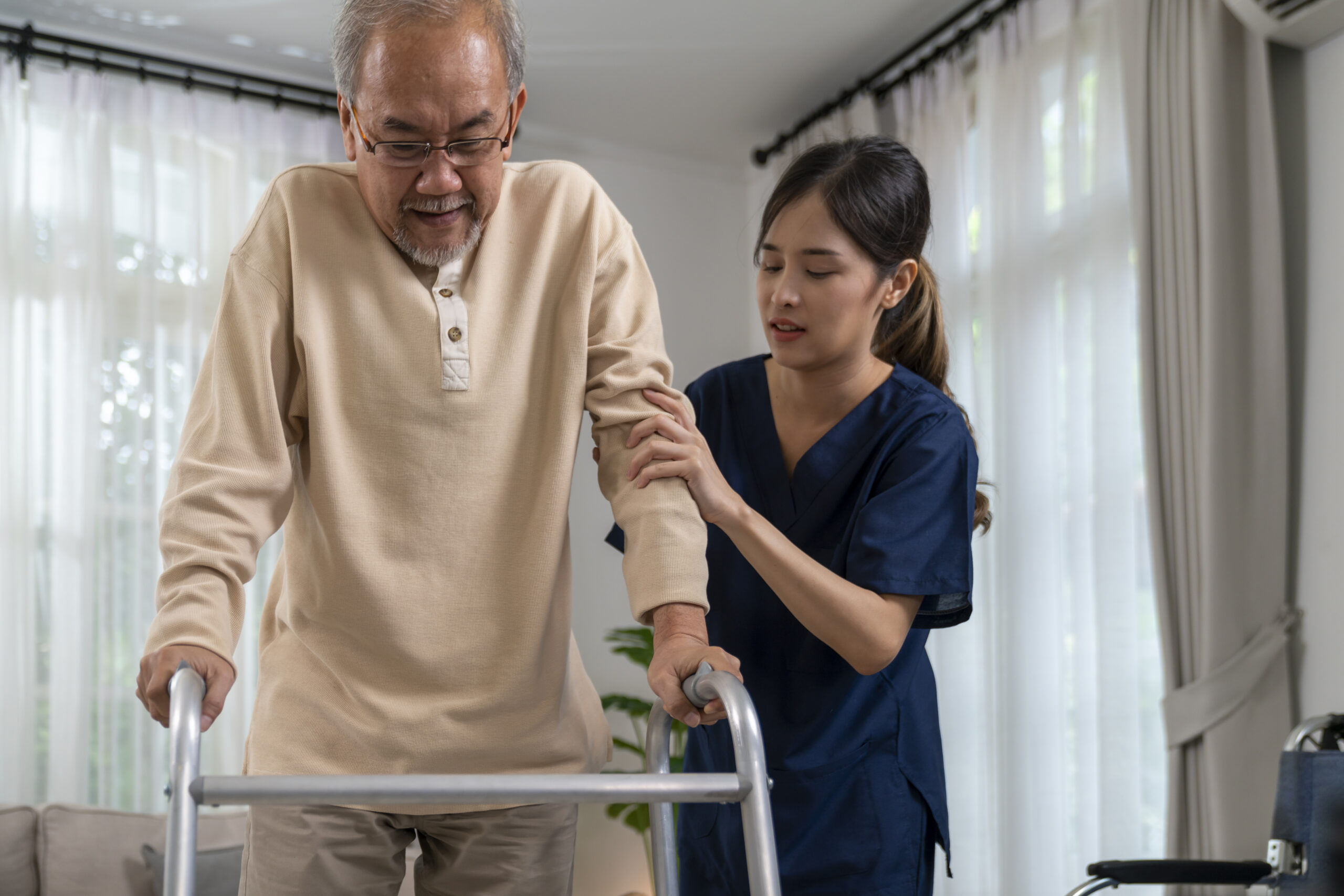 An elderly person using a walker with the assistance of a caregiver. Alt text: "Elderly individual improving mobility with the aid of a walker and caregiver support.